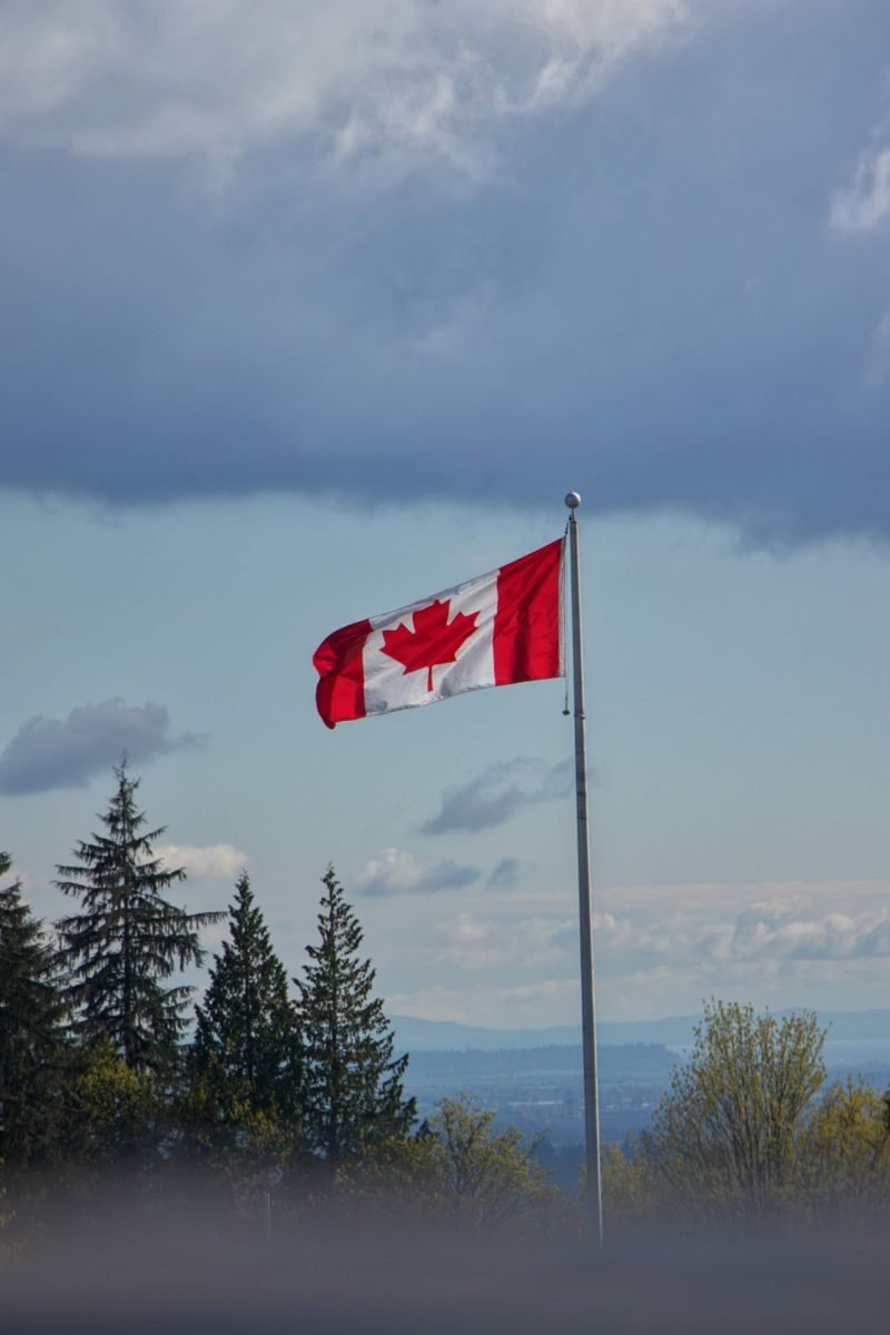 A Canadian flag on a flagpole waving under a cloudy sky. Symbol of national pride and patriotism.