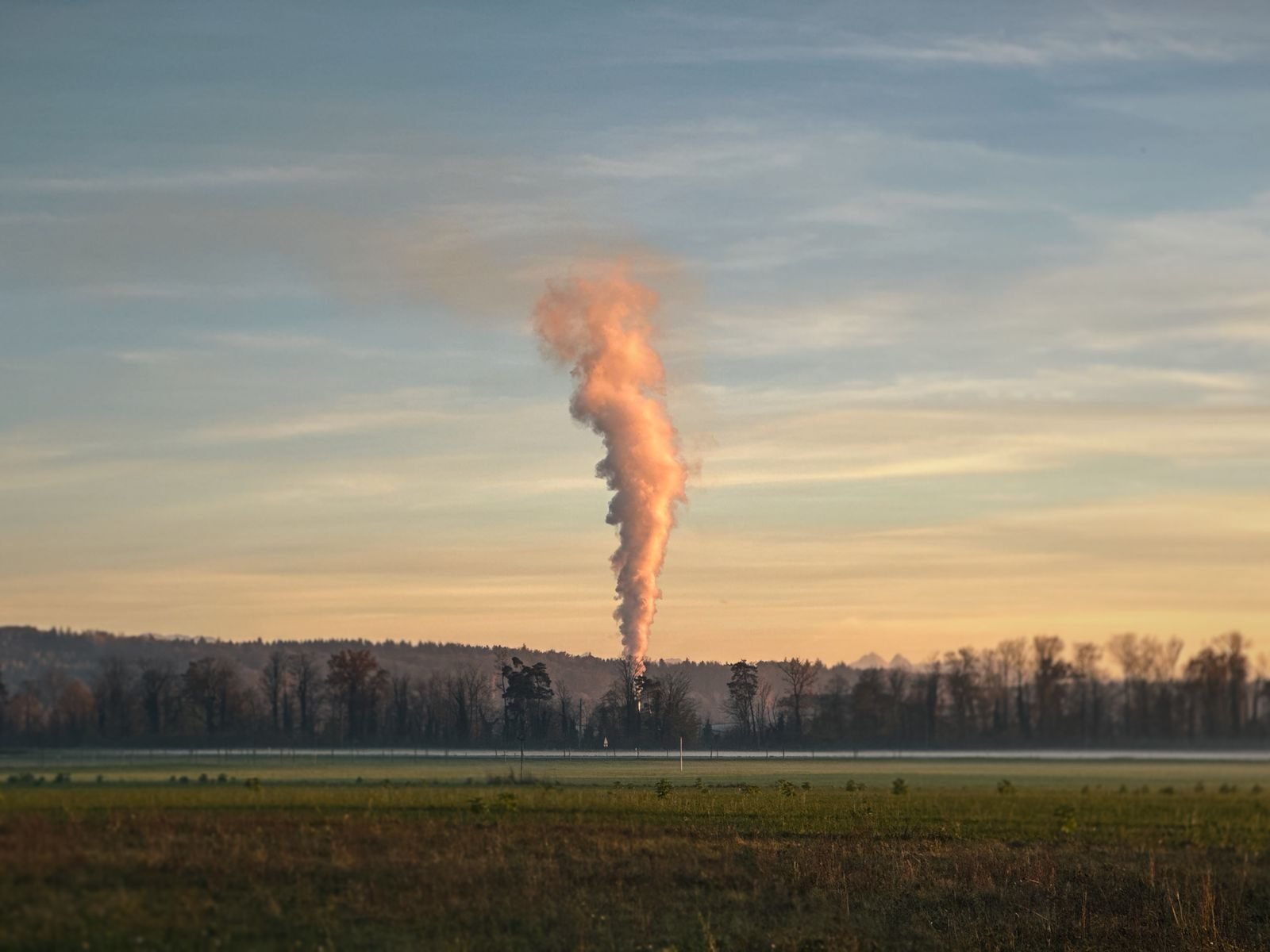 Smoke rises into the sky over a foggy field at sunrise, creating a dramatic view.