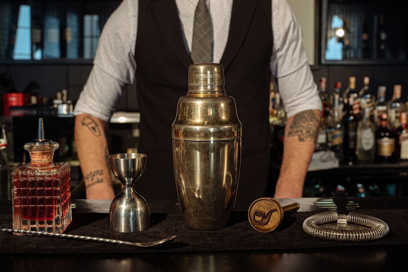 A bartender's setup featuring a cocktail shaker and bar tools on a counter, ready for mixing.