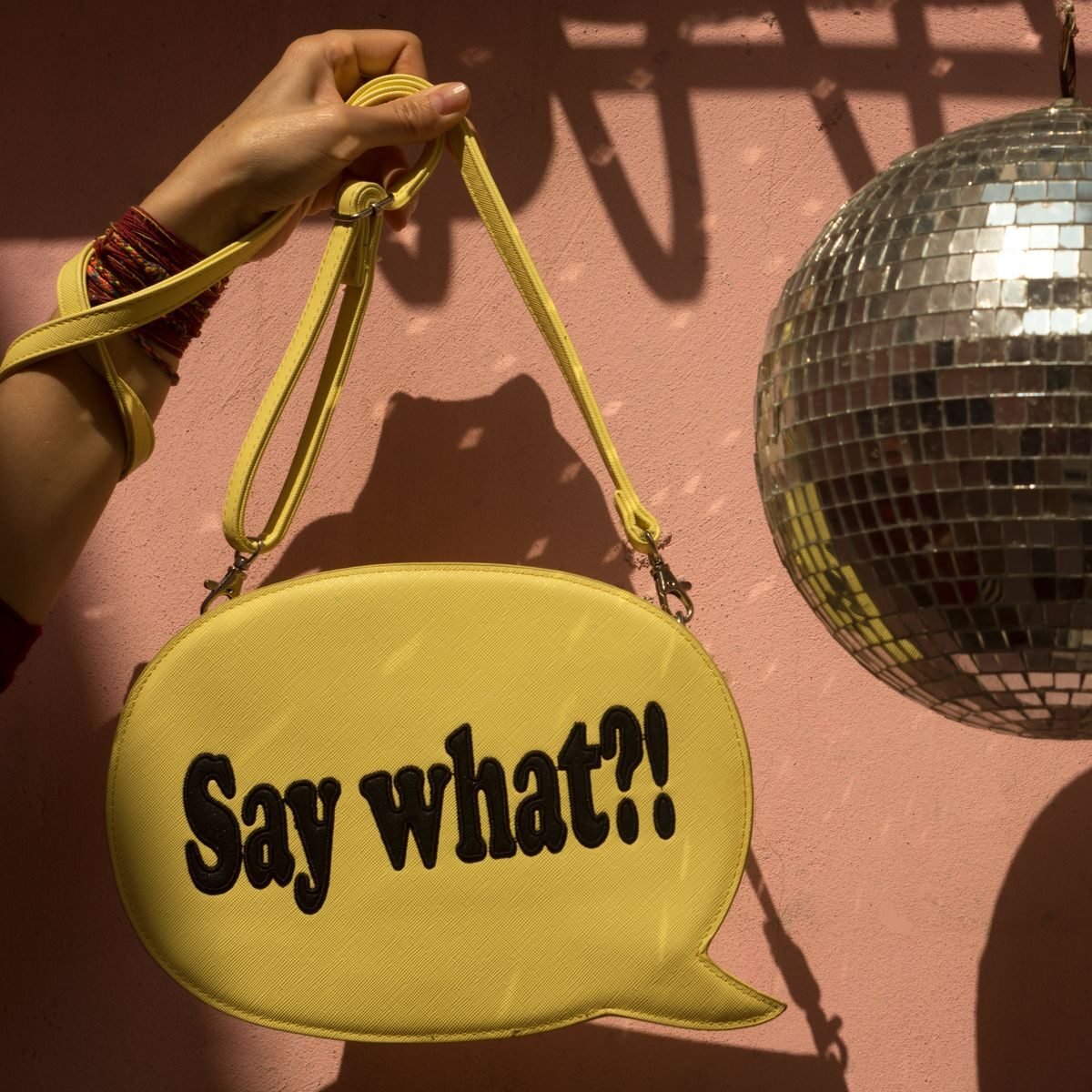 Vibrant yellow bag with 'Say what?!' text against a pink wall and disco ball.