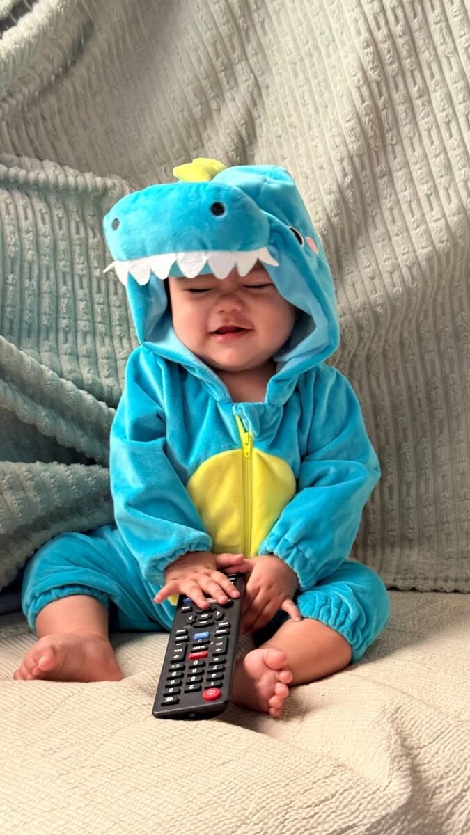 Baby in dinosaur costume holding a remote control.