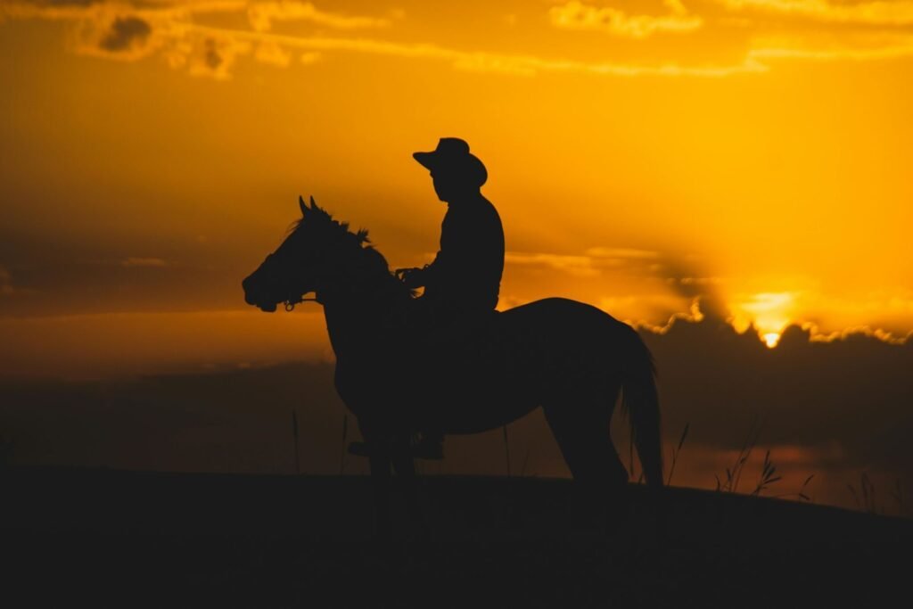 A cowboy rides a horse in silhouette against a stunning sunset sky, evoking adventure.