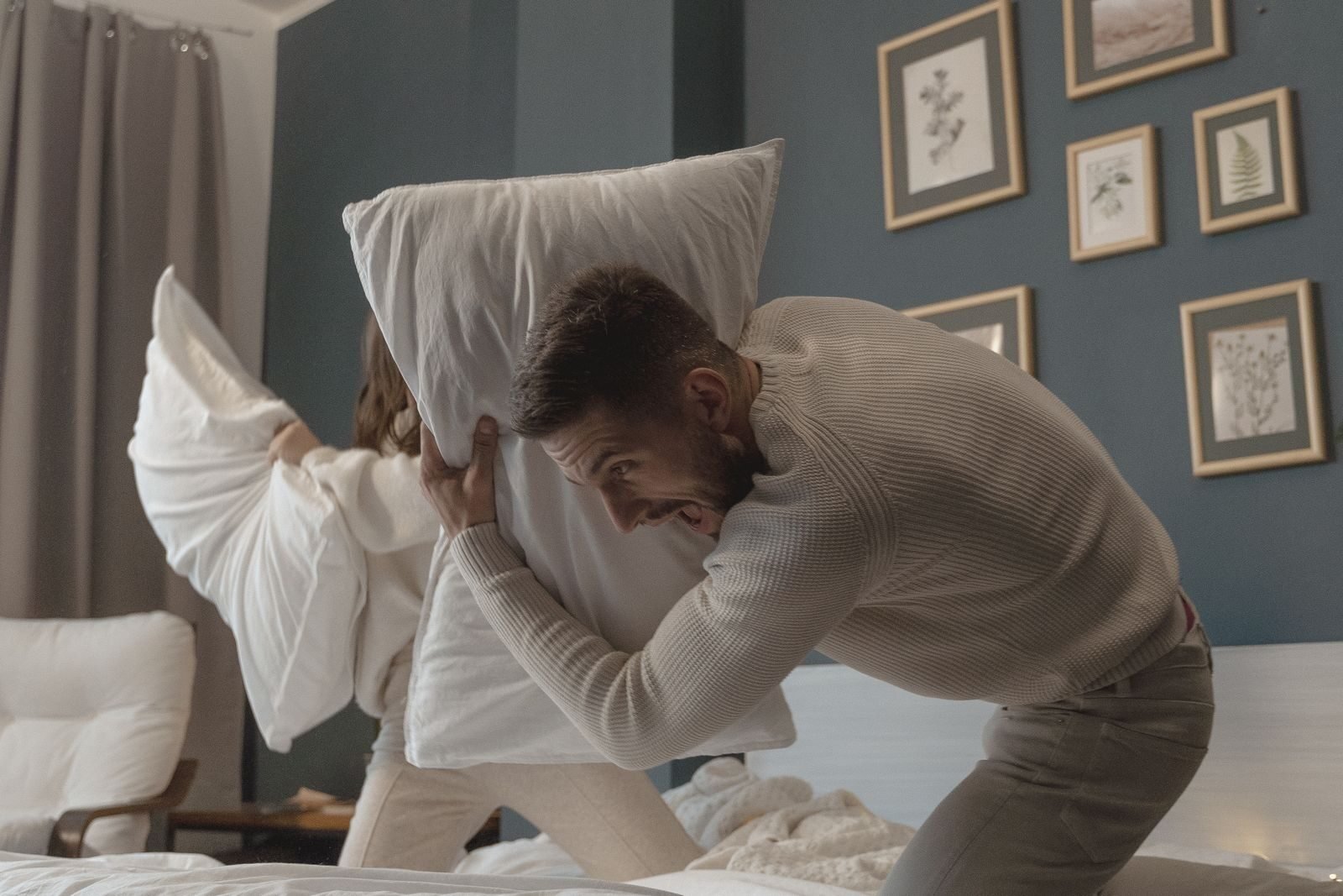 Couple enjoying a playful pillow fight in a cozy bedroom. Warm tones and joyful expressions.