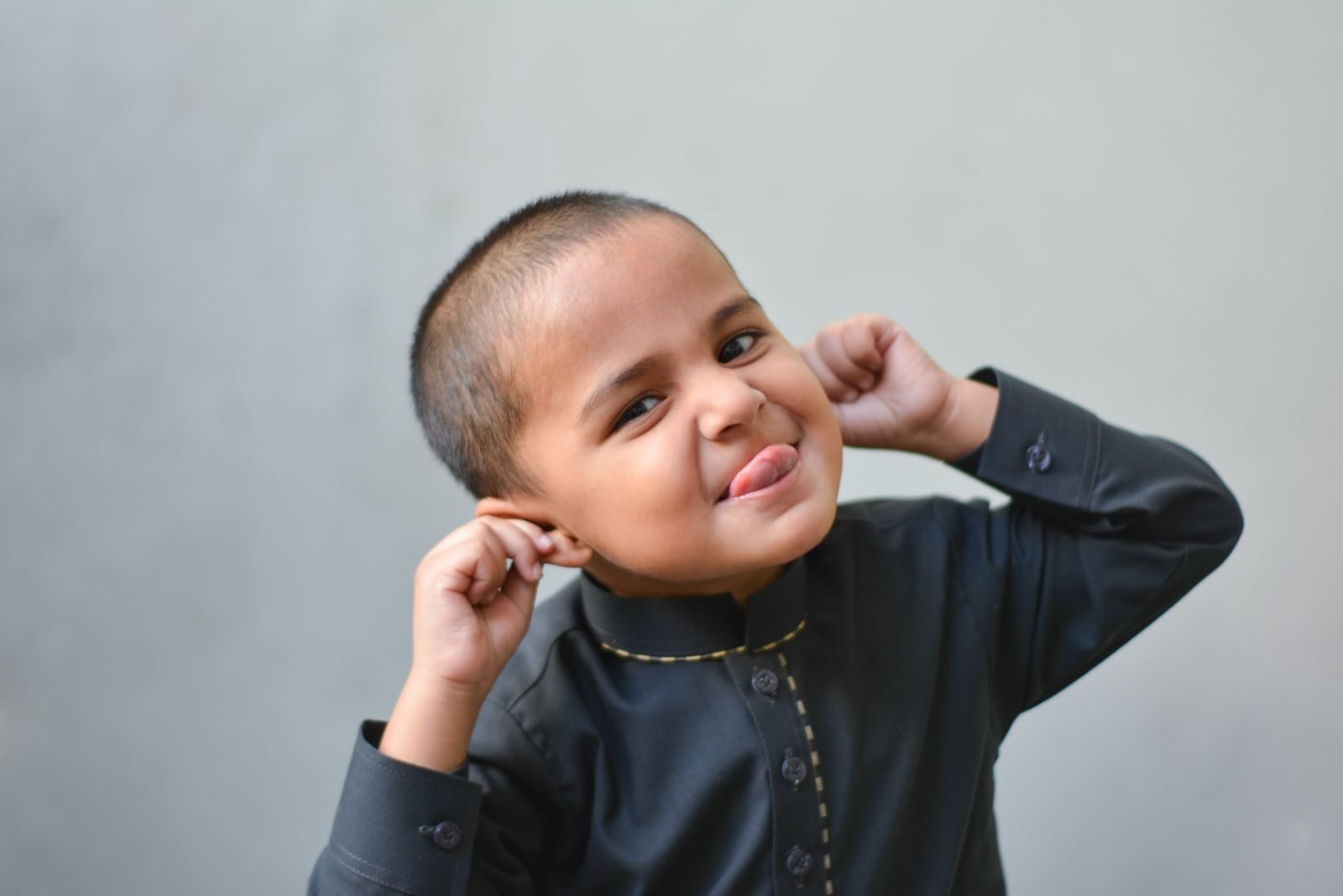 A cheerful child in traditional attire playfully makes a face against a plain background.