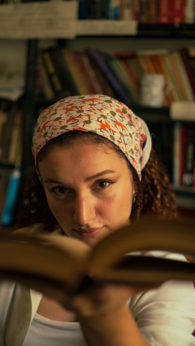 Portrait of a woman wearing a headscarf reading a book in a cozy library setting.