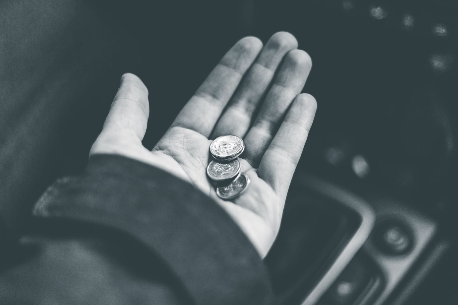Black and white crop anonymous person demonstrating shiny coins while sitting in car on blurred background