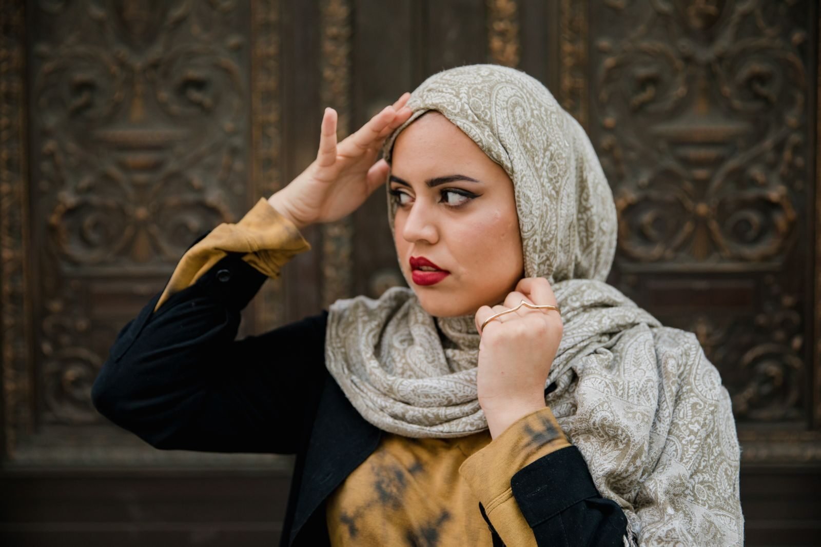 Elegant woman in a patterned hijab, posing outdoors against a textured background.