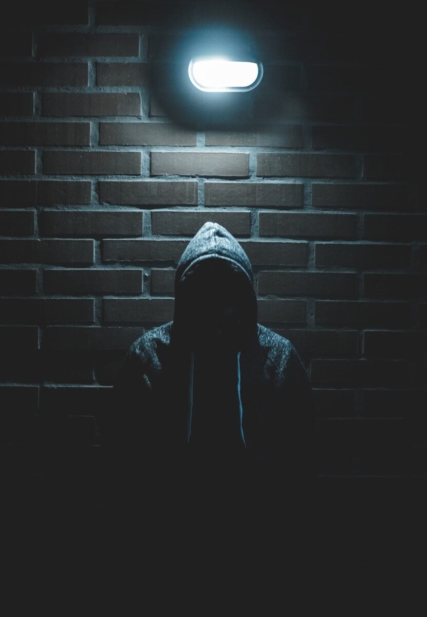 A person in a hooded sweatshirt in silhouette against a dark brick wall