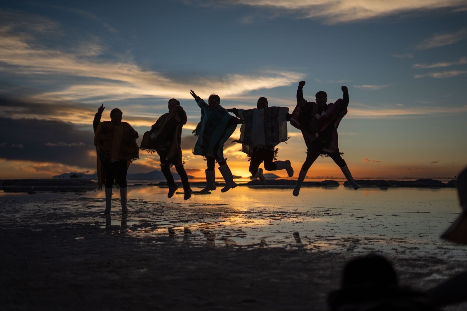 Group of people jumping joyfully at sunset over reflective water.
